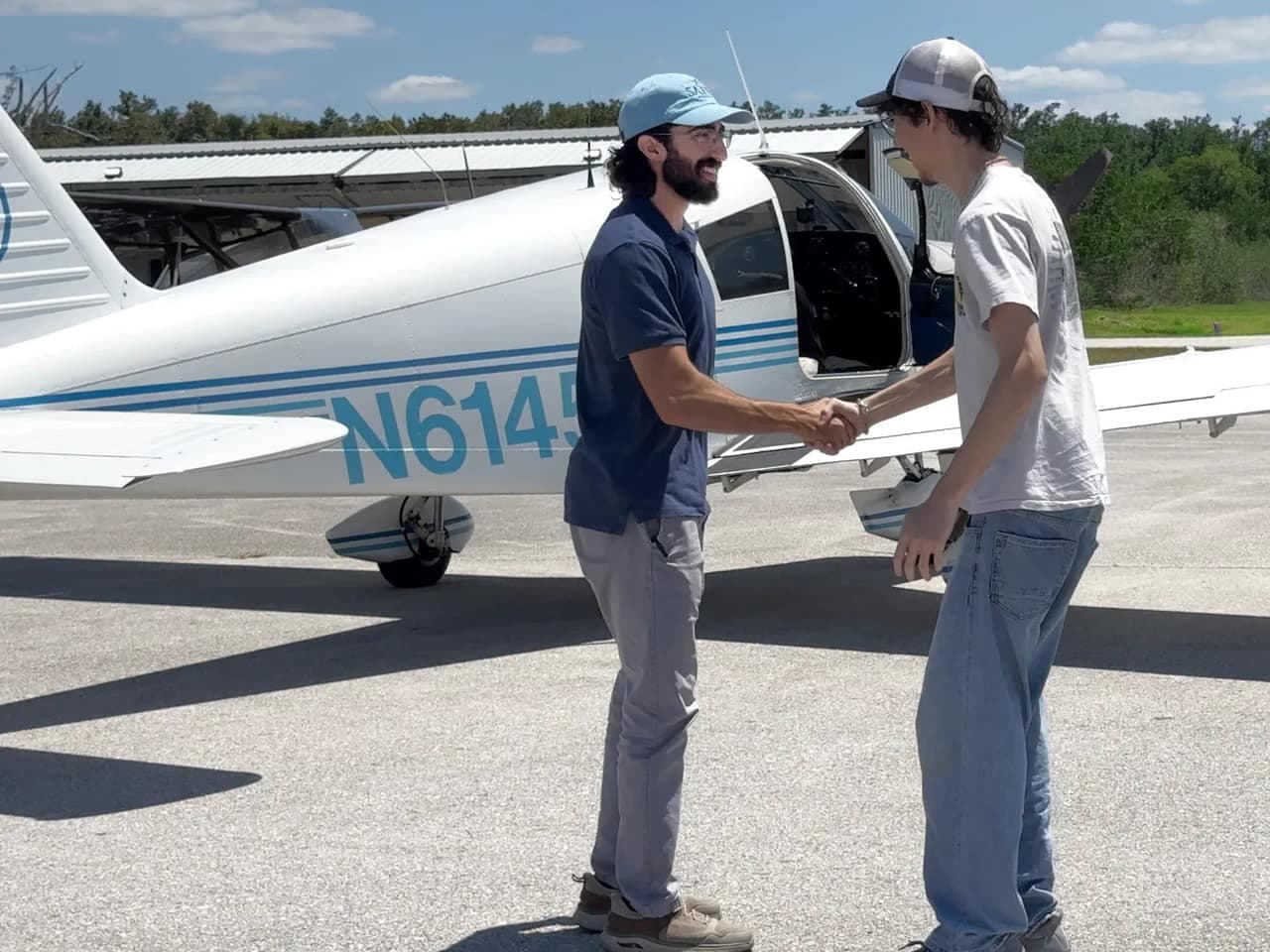A Core Aviator Training instructor shaking hands with a student beside the school’s Piper Cherokee 140 on the ramp.