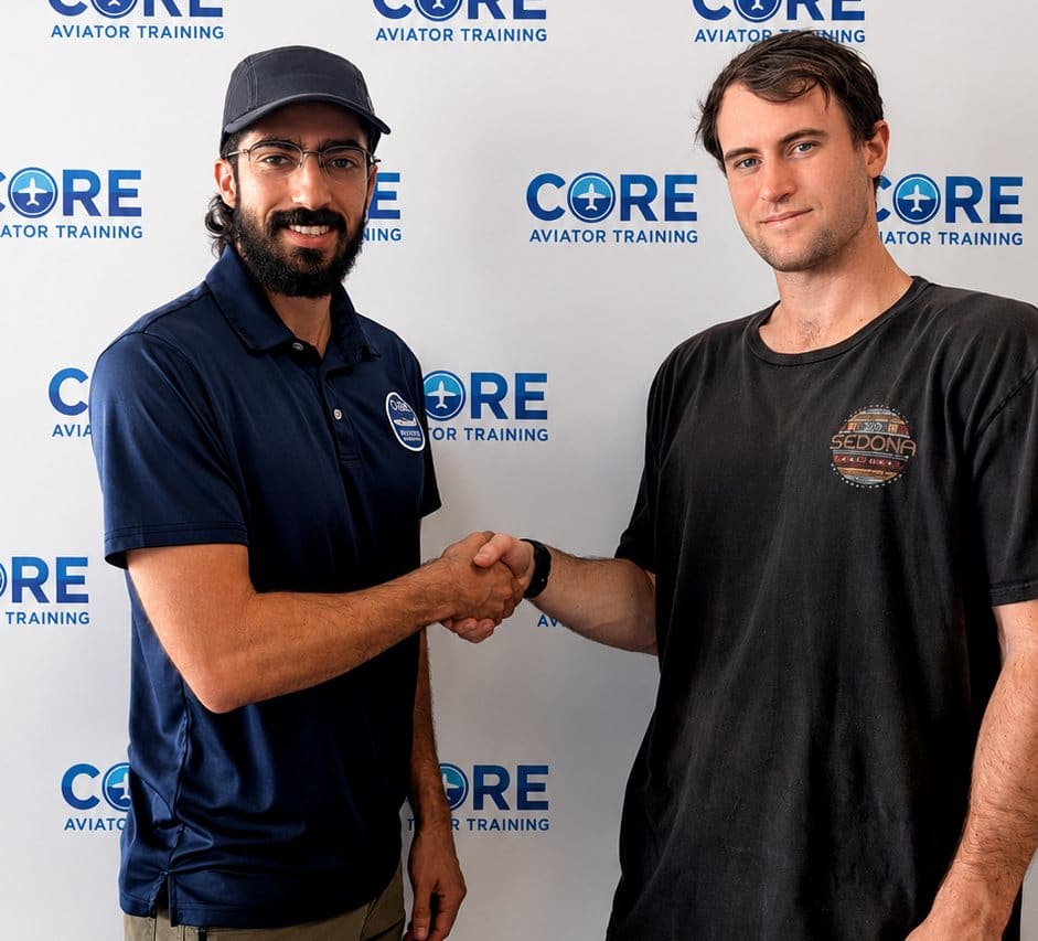 A Core Aviator Training instructor congratulating a student pilot in front of the school’s banner.